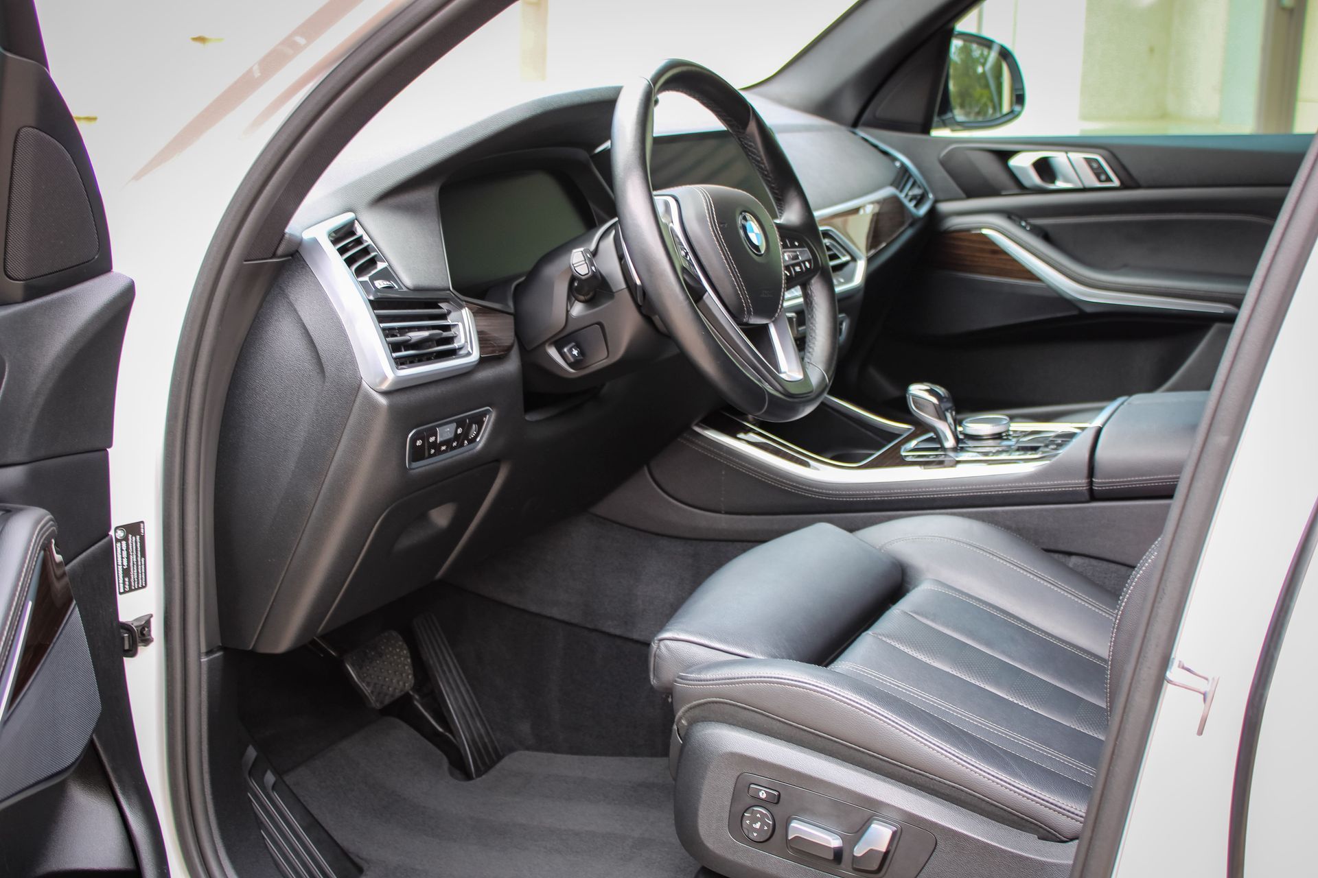Interior of a white BMW SUV, driver's side view. Black leather seat, dashboard, steering wheel, and silver trim.