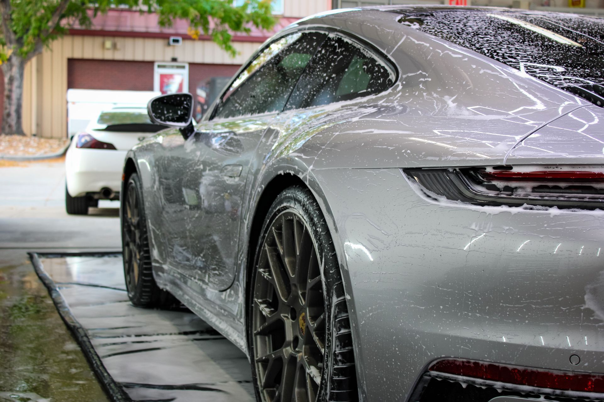 Silver Porsche 911 being washed at a car wash, covered in soapy foam.