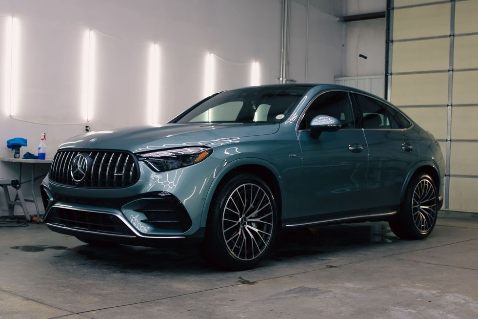 Green Mercedes-Benz SUV coupe in a car detailing bay, with black grille and wheels, under bright lights.