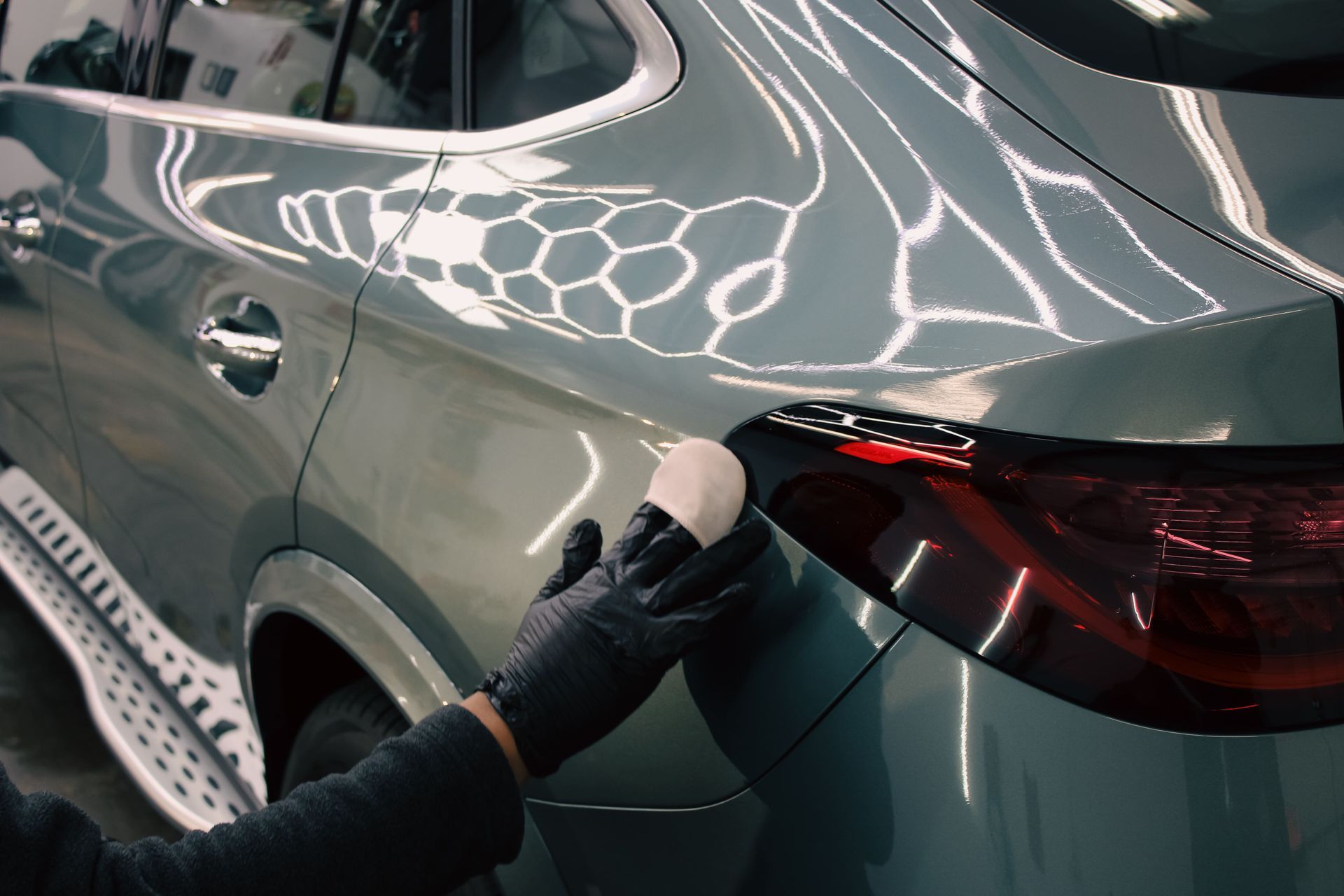 Person wearing black gloves claying a silver SUV, showing a reflective hexagonal pattern on the paint.