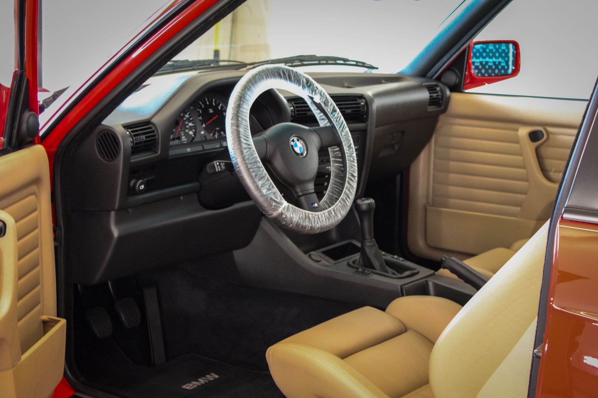 Red BMW car interior with tan seats and black dashboard. Steering wheel covered.