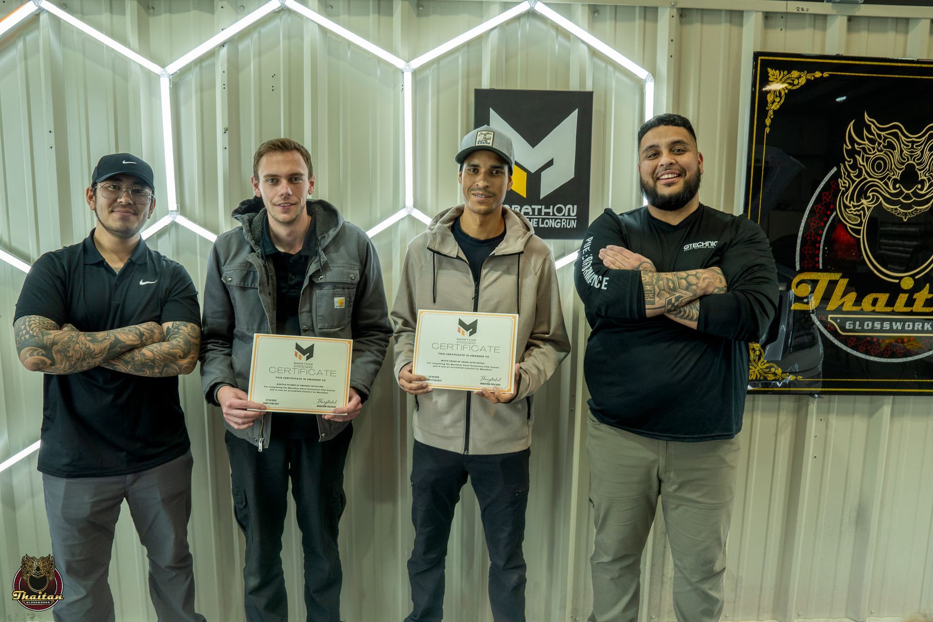 Four people holding framed awards, standing in front of a logo and a Thai boxing sign.