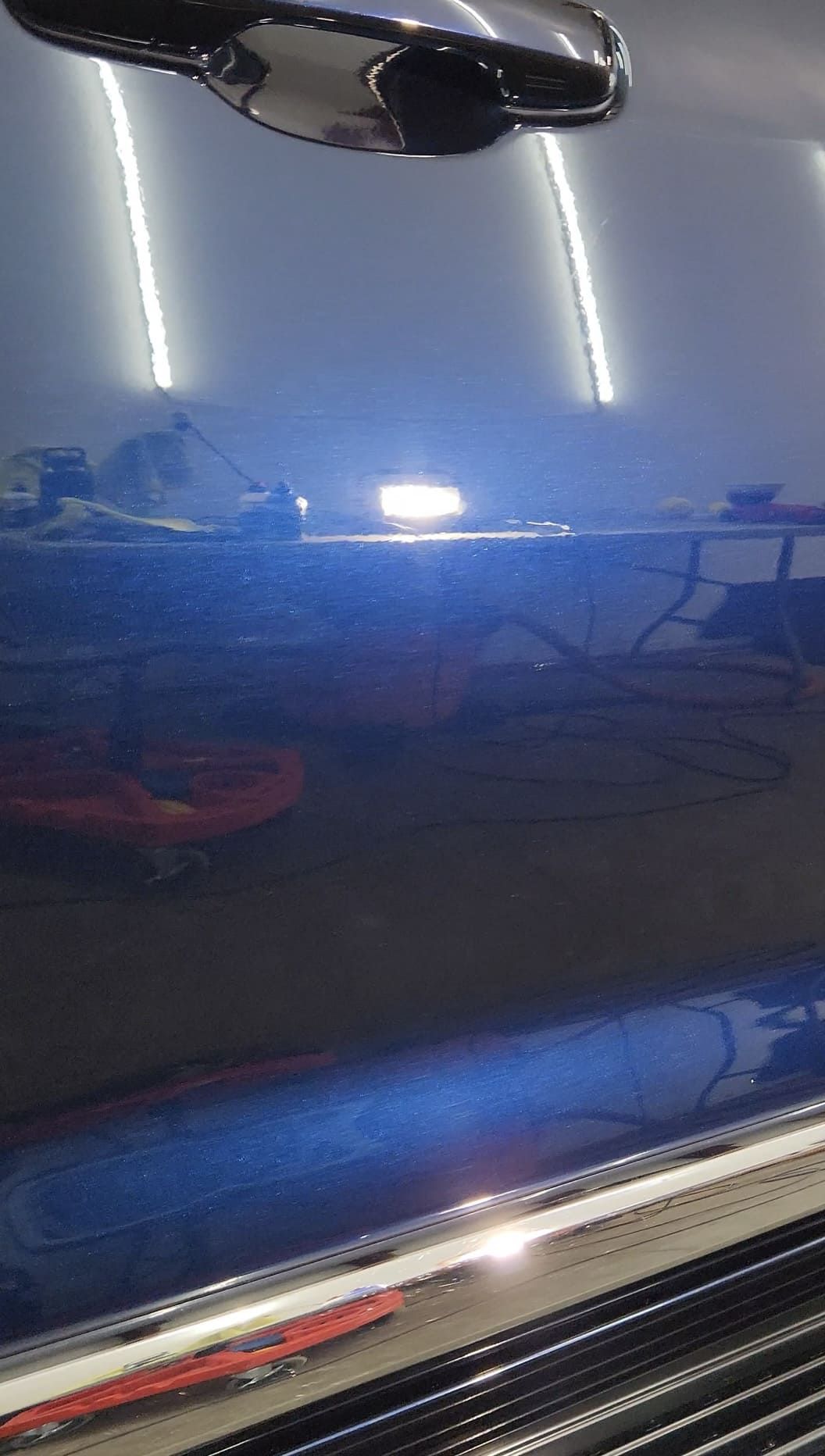 Blue car door reflecting bright overhead lights.