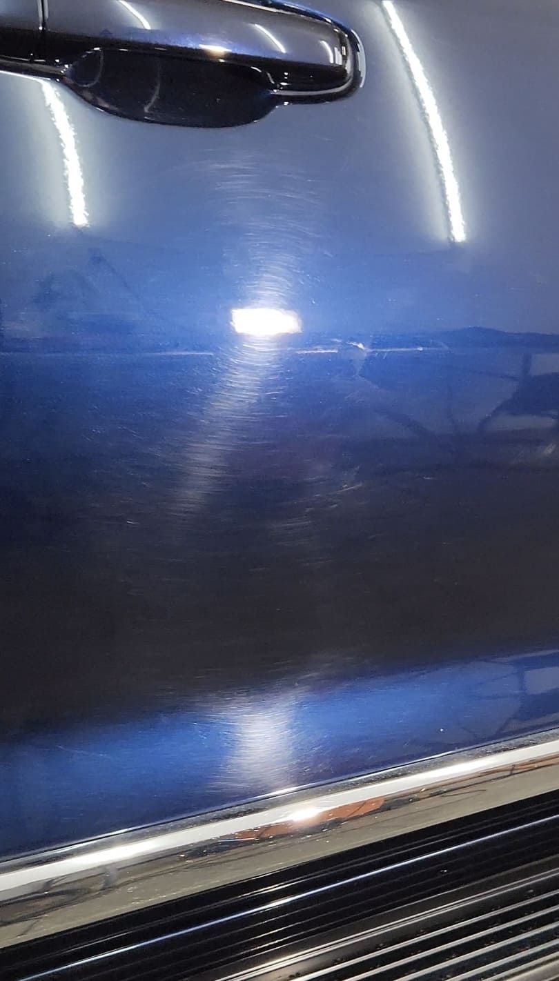 Blue car door with swirl marks under bright lights. Chrome door handle.
