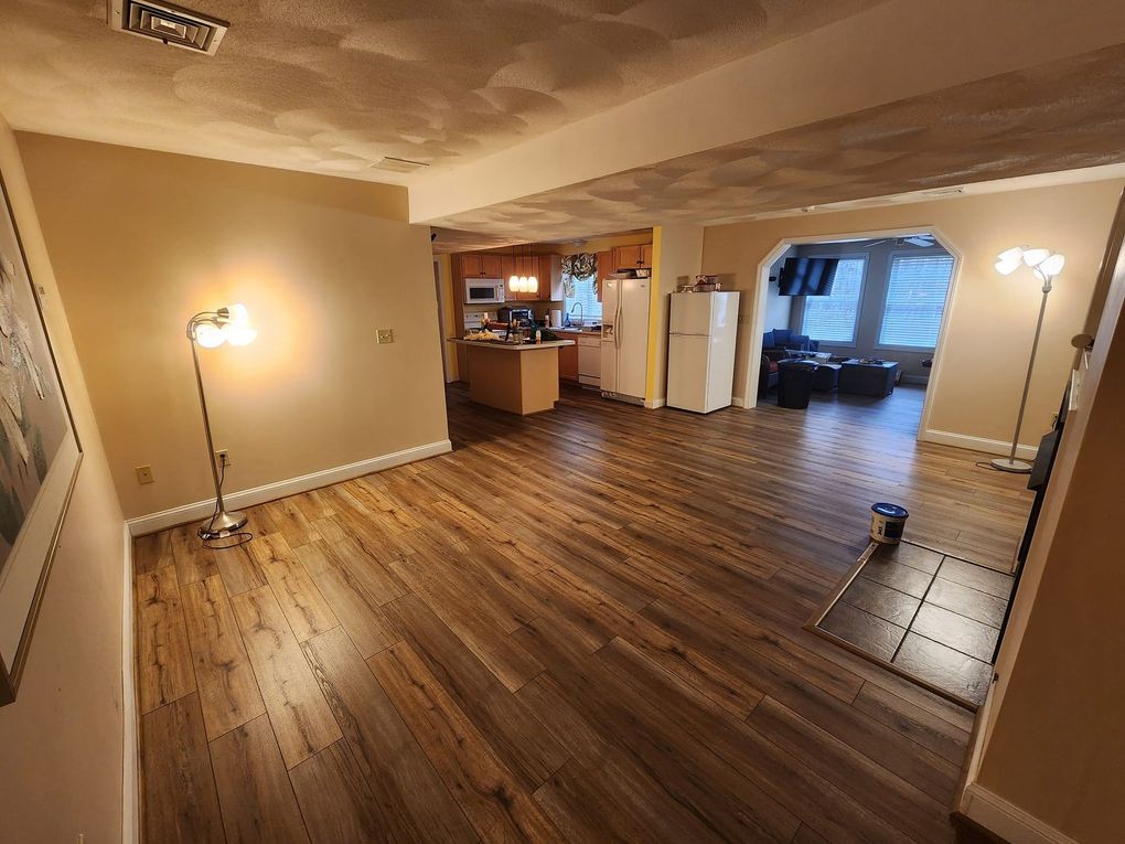 A living room with hardwood floors and a kitchen in the background.