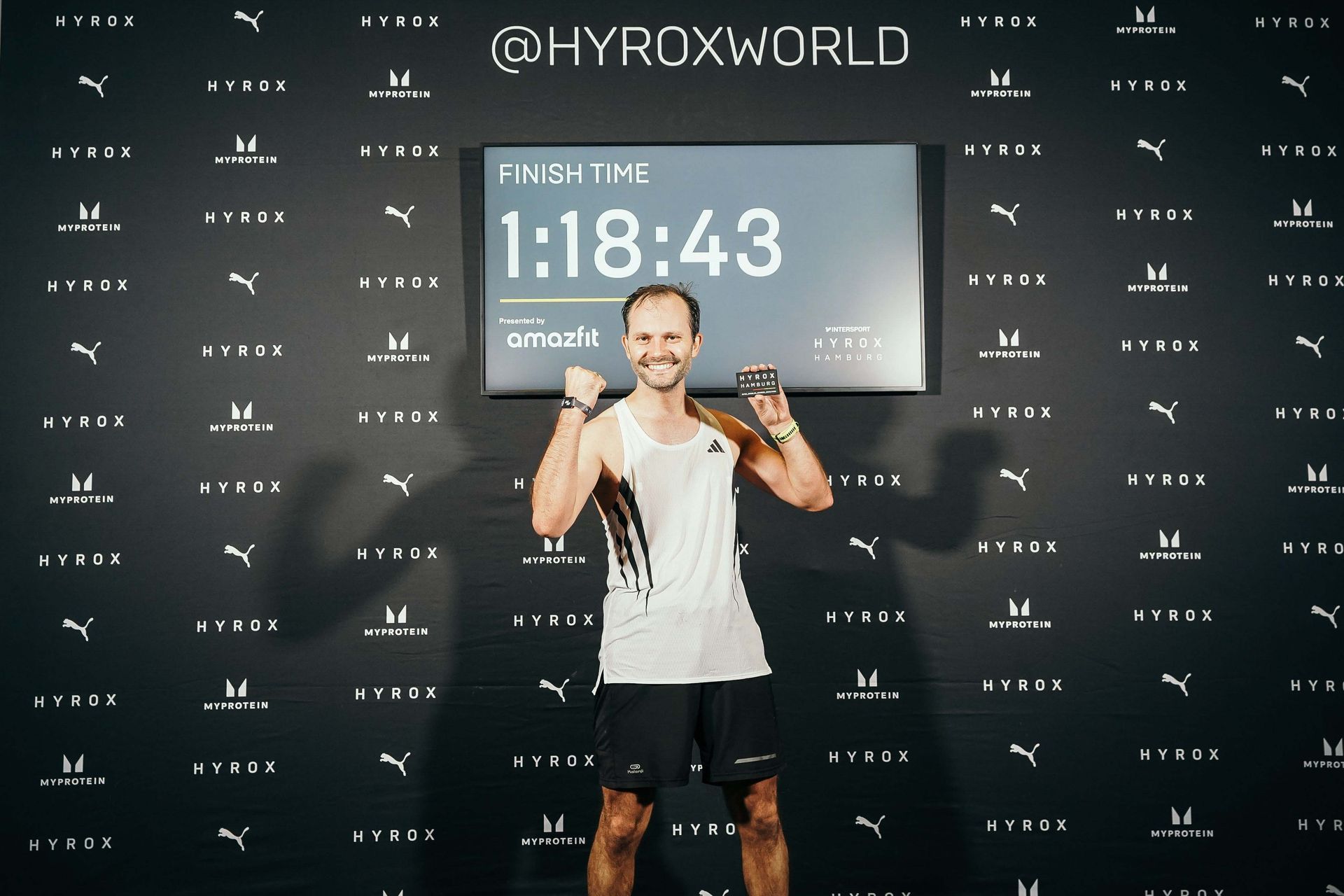 Ein Mann im weißen Tanktop vor der Finisher Wall beim HYROX Hamburg 2025