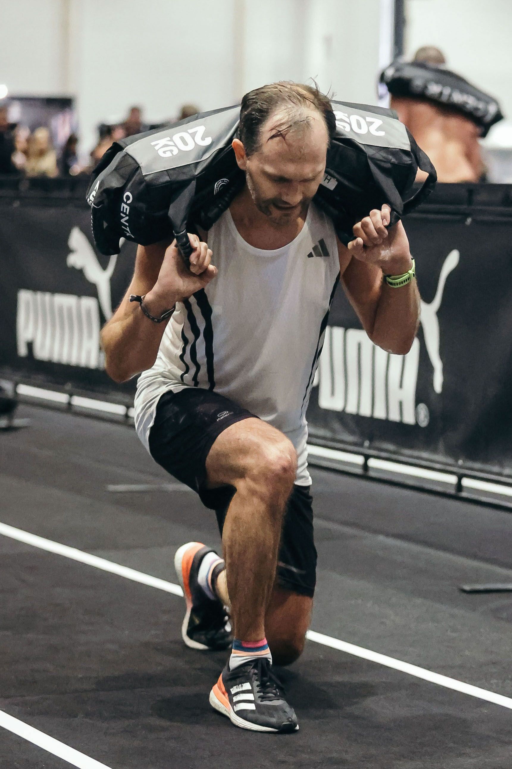 Ein Mann im weißen Tanktop bei der HYROX Übung Sandbag Lunges