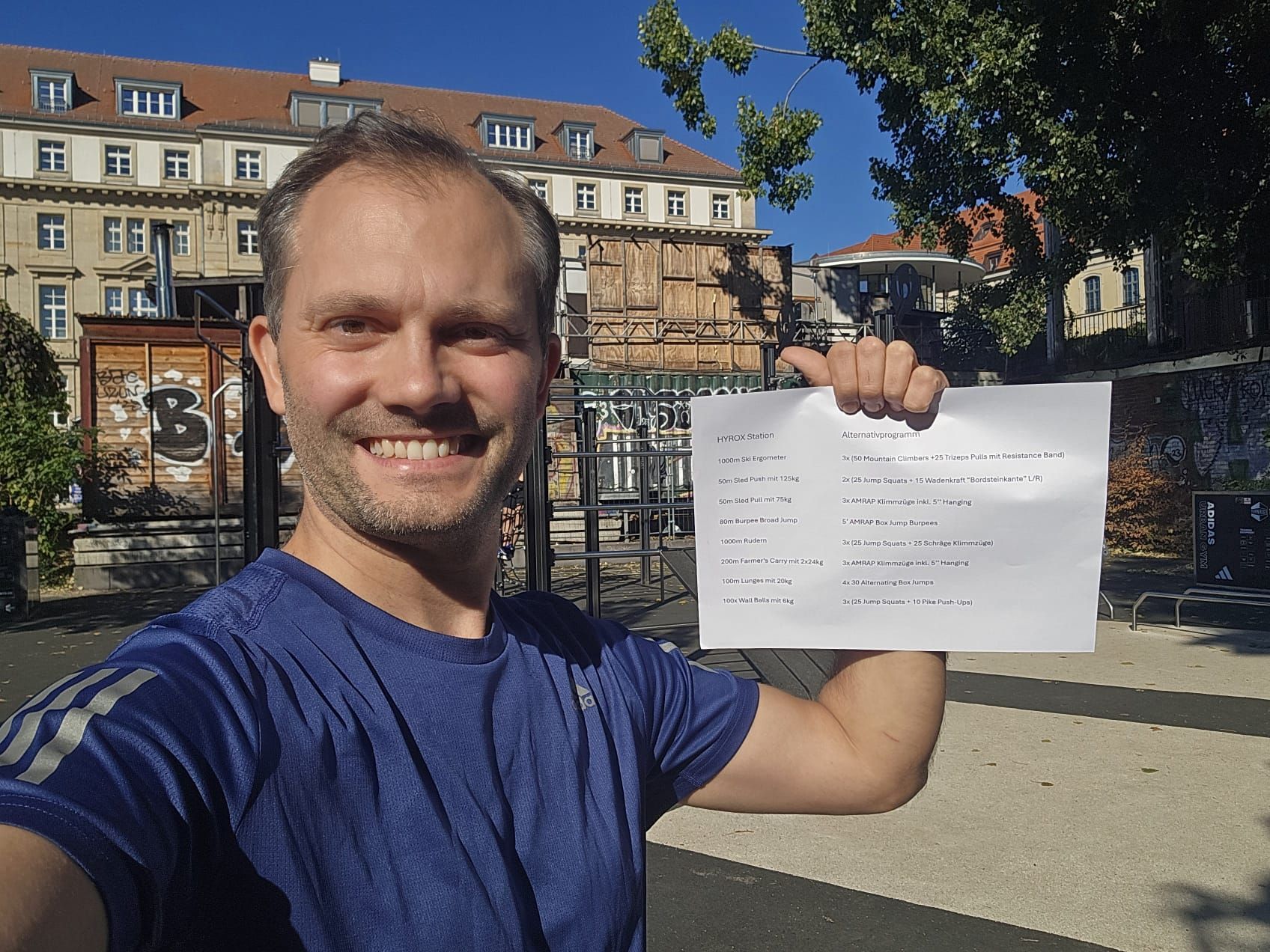 Ein Mann im blauen T-Shirt hält einen bedrucken weißen Zettel hoch