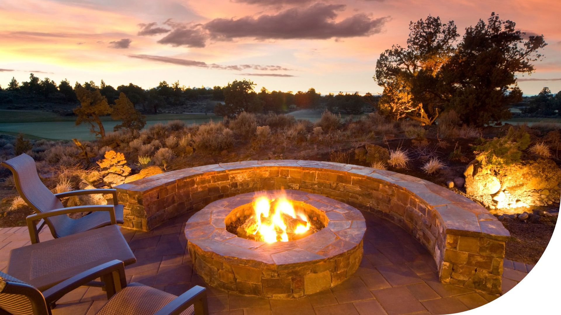 Fire pit with curved stone seating on a patio at sunset.