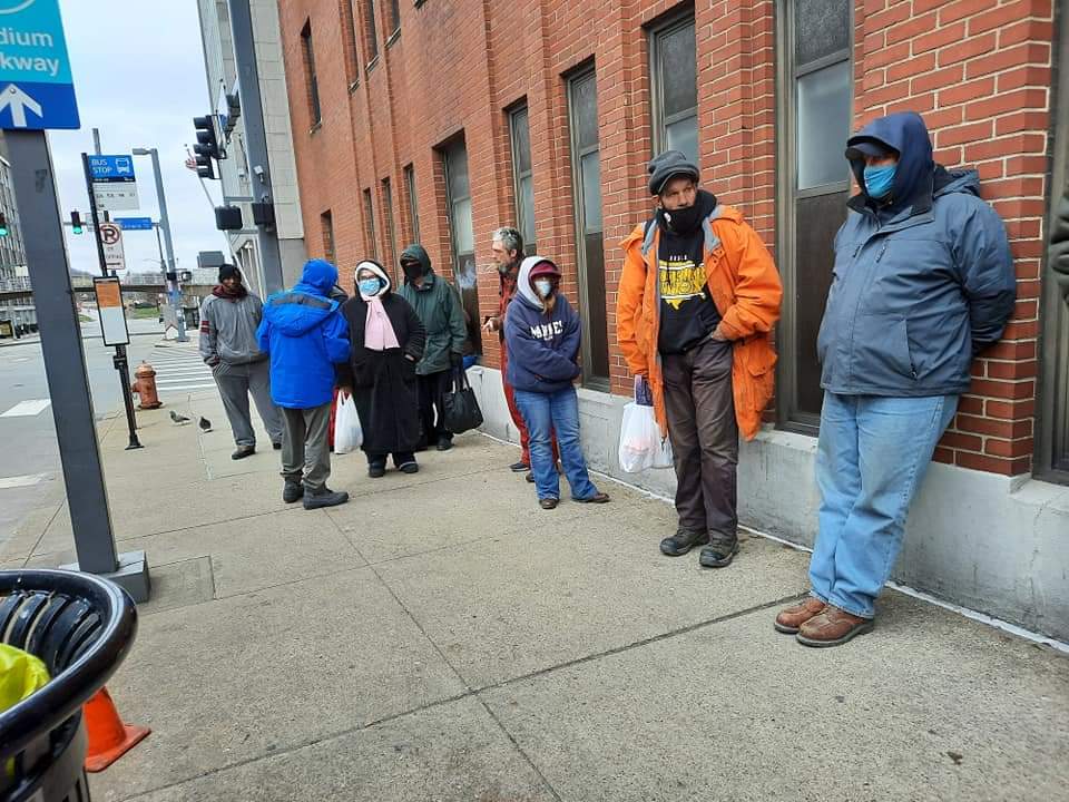 A group of people wearing masks are standing on a sidewalk.