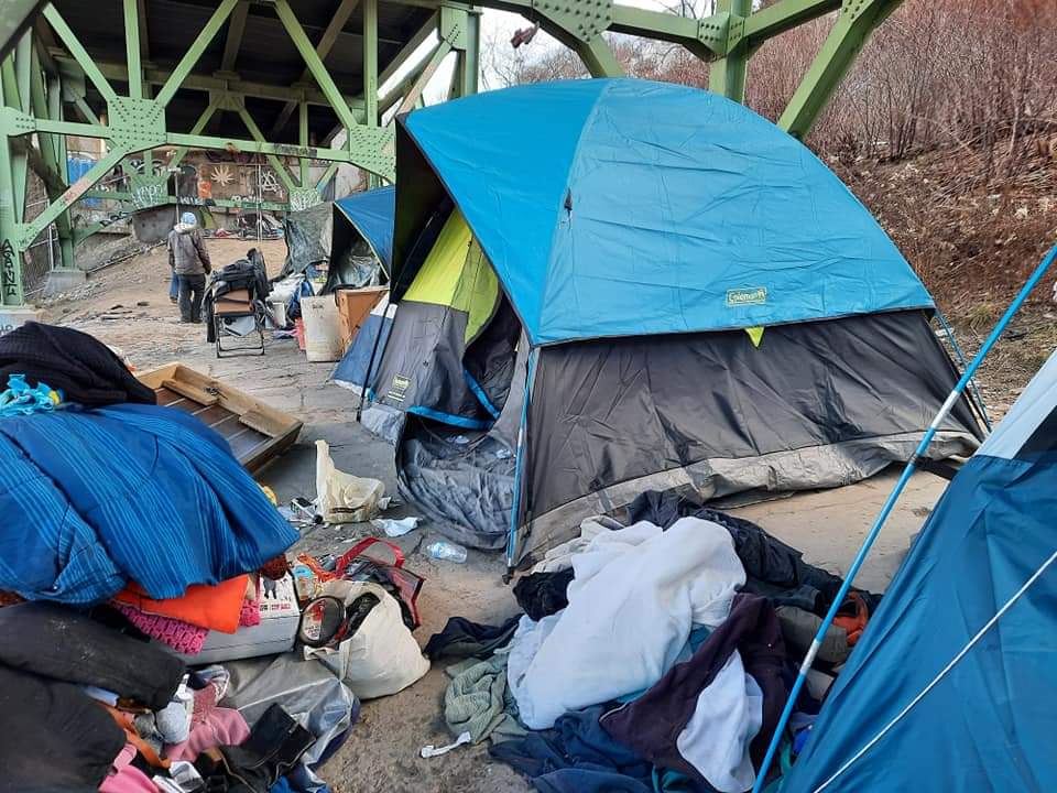 A group of tents are sitting under a bridge.