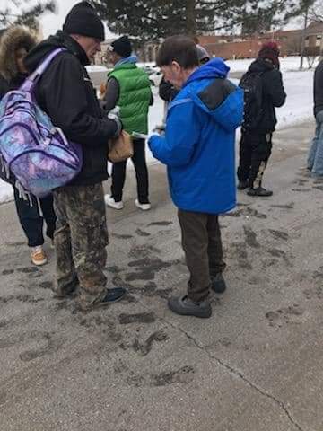 A group of people are standing on a sidewalk in the snow.