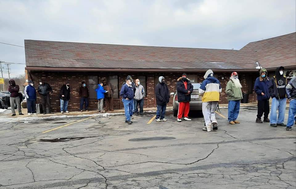 A group of people are standing in a parking lot in front of a building.