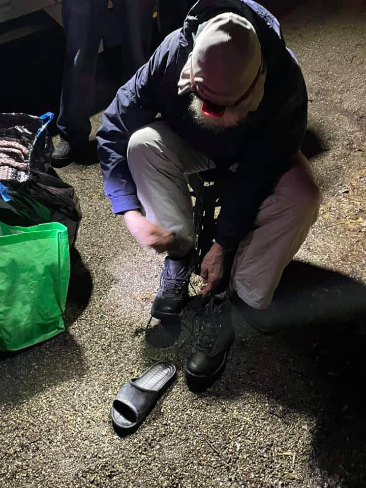 A man is kneeling down on the ground tying his shoes.