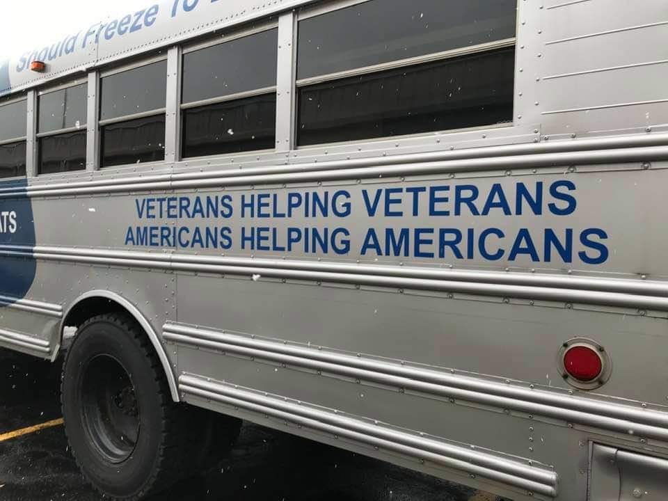 A bus that says veterans helping veterans americans helping americans is parked in a parking lot.