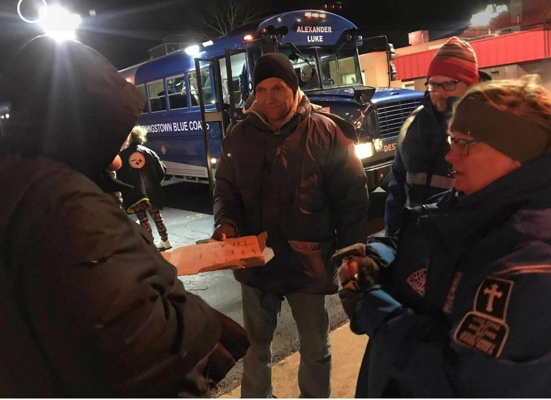 A group of people standing in front of a blue bus with the word emergency on it