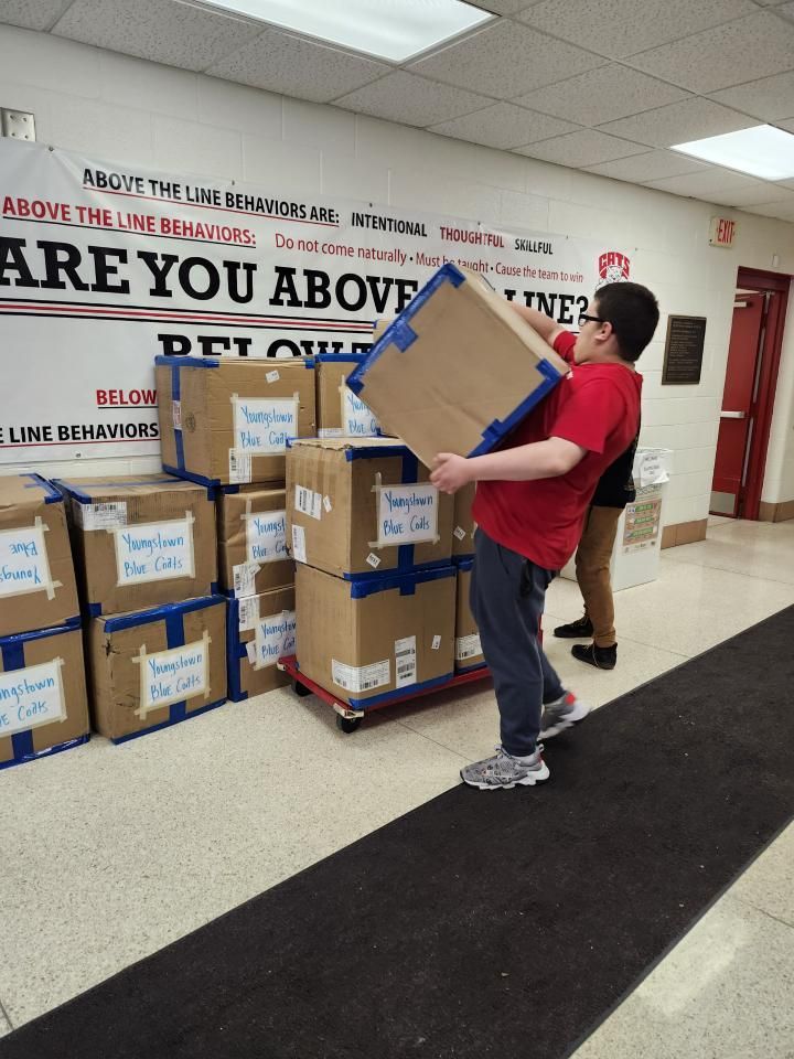 A man is carrying a box in front of a wall that says
