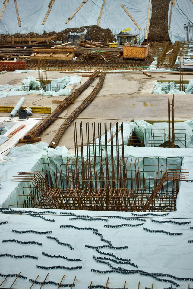 Construction site showing steel rebar reinforcement cages and structural foundations on a white base under a tent.