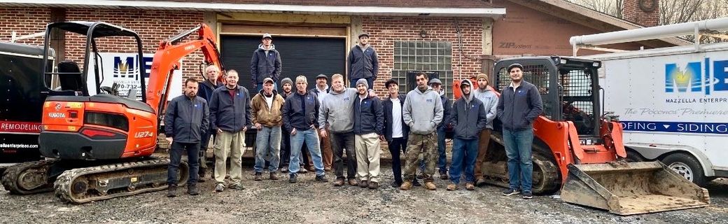 Crew posing in front of a brick house beside orange and white work trucks and equipment.