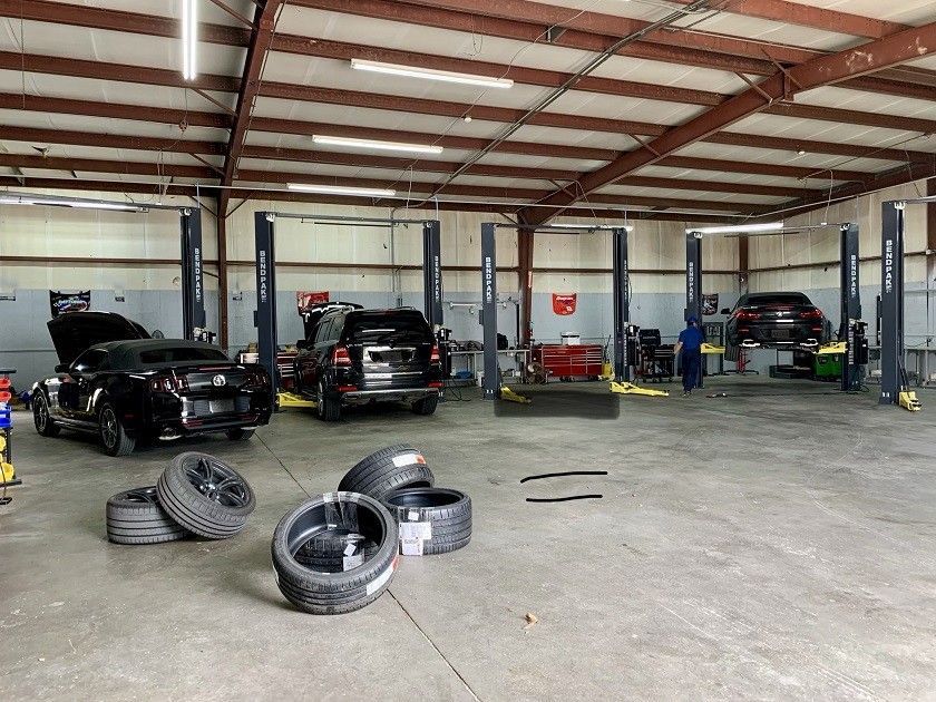 A garage with cars on lifts and tires on the floor.