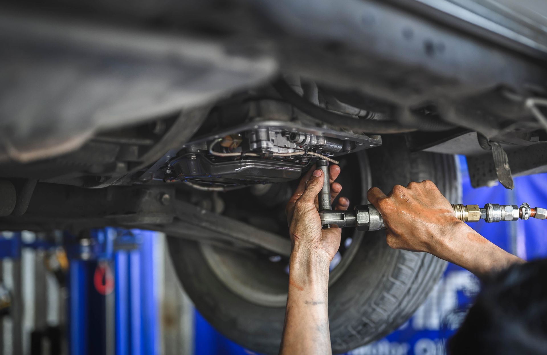 A man is working on the underside of a car in a garage.