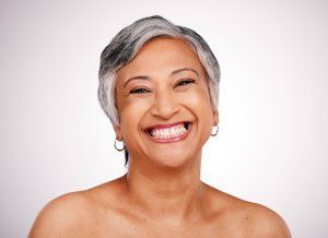 Woman with short gray hair smiling, wearing hoop earrings, against a white backdrop.