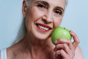 Smiling woman with white hair, holding a green apple.