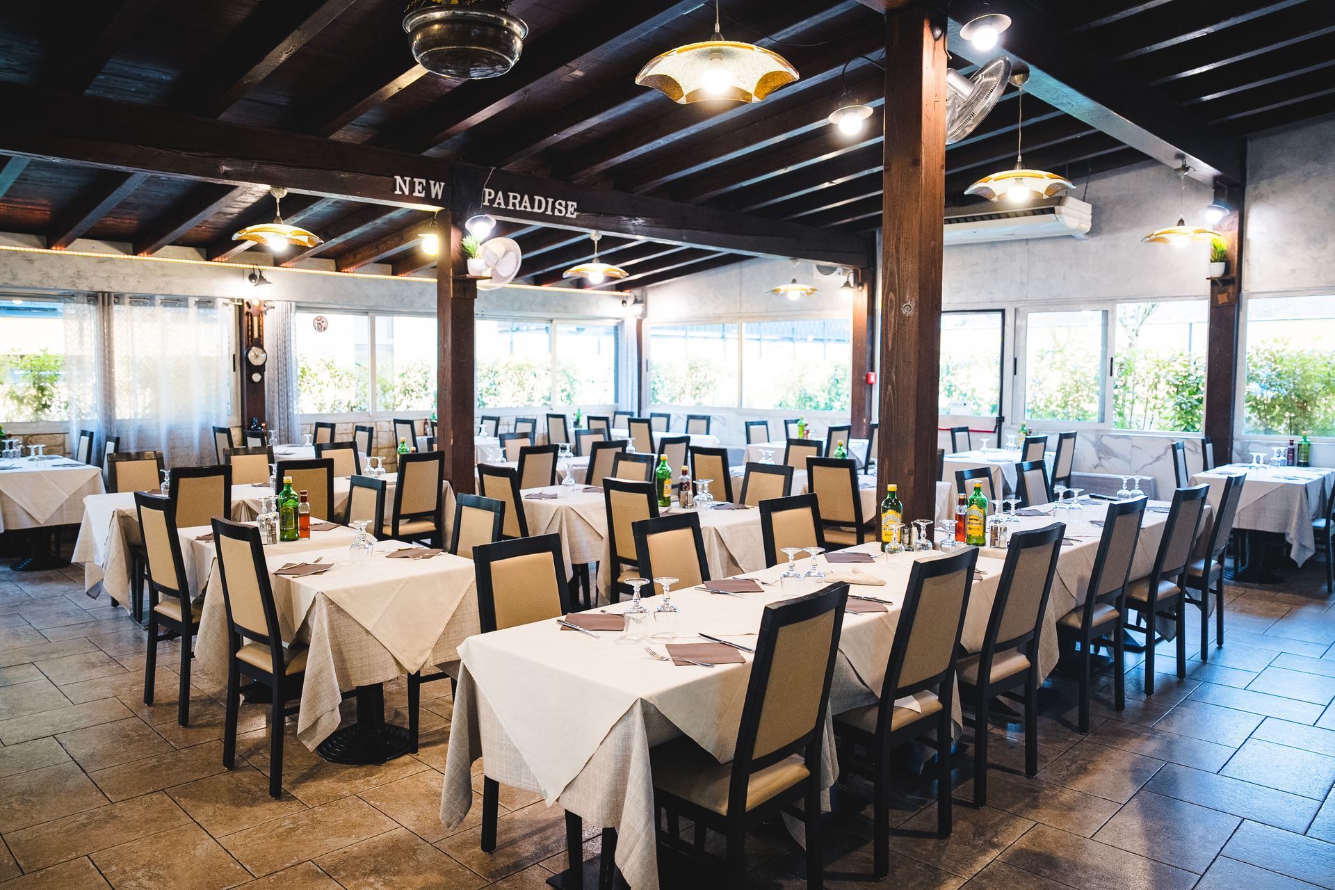 Interno del ristorante con tavoli coperti da tovaglie bianche, travi in ​​legno e sedie disposte per i commensali.