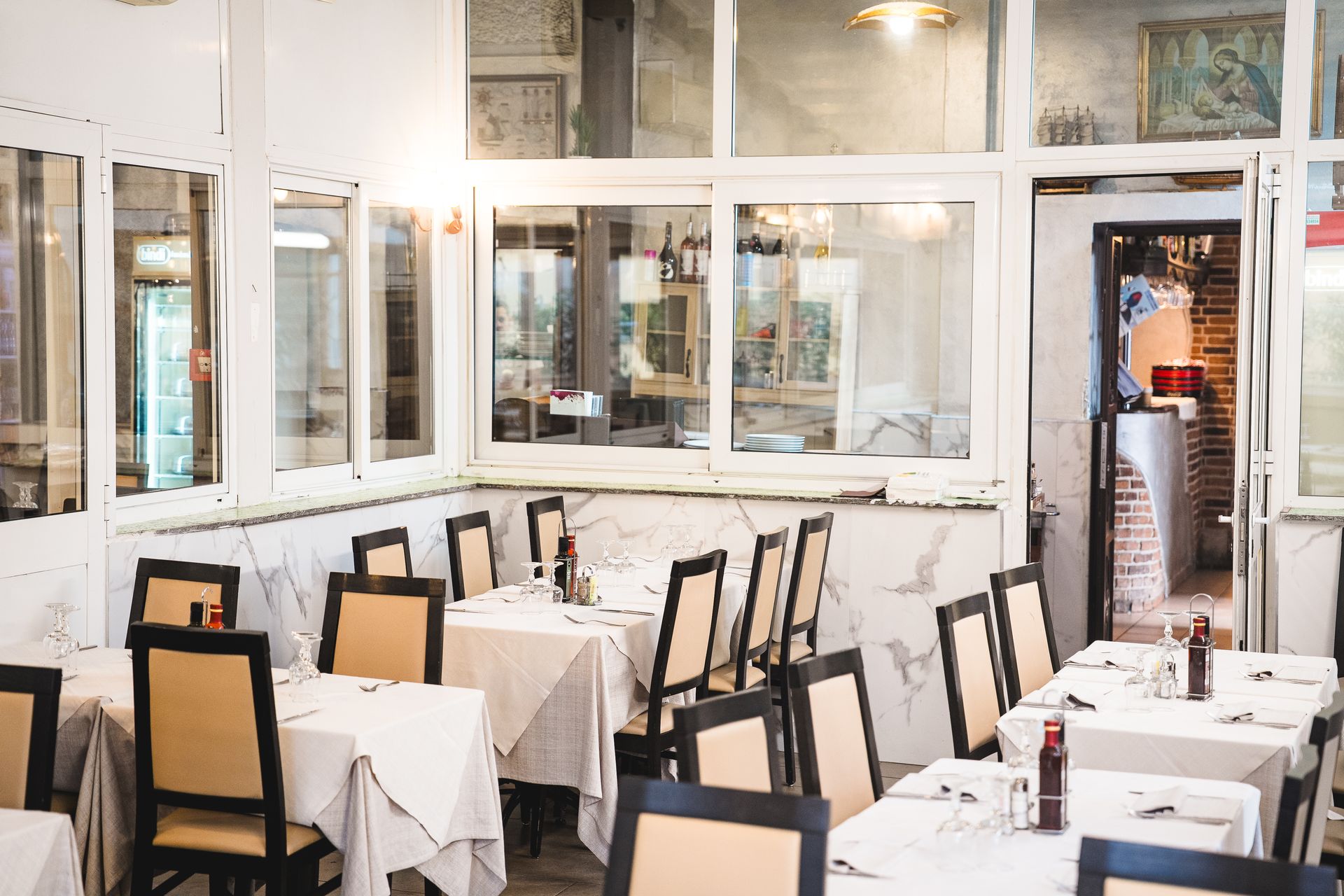 Sala da pranzo vuota del ristorante con tovaglie bianche, sedie e grandi finestre.