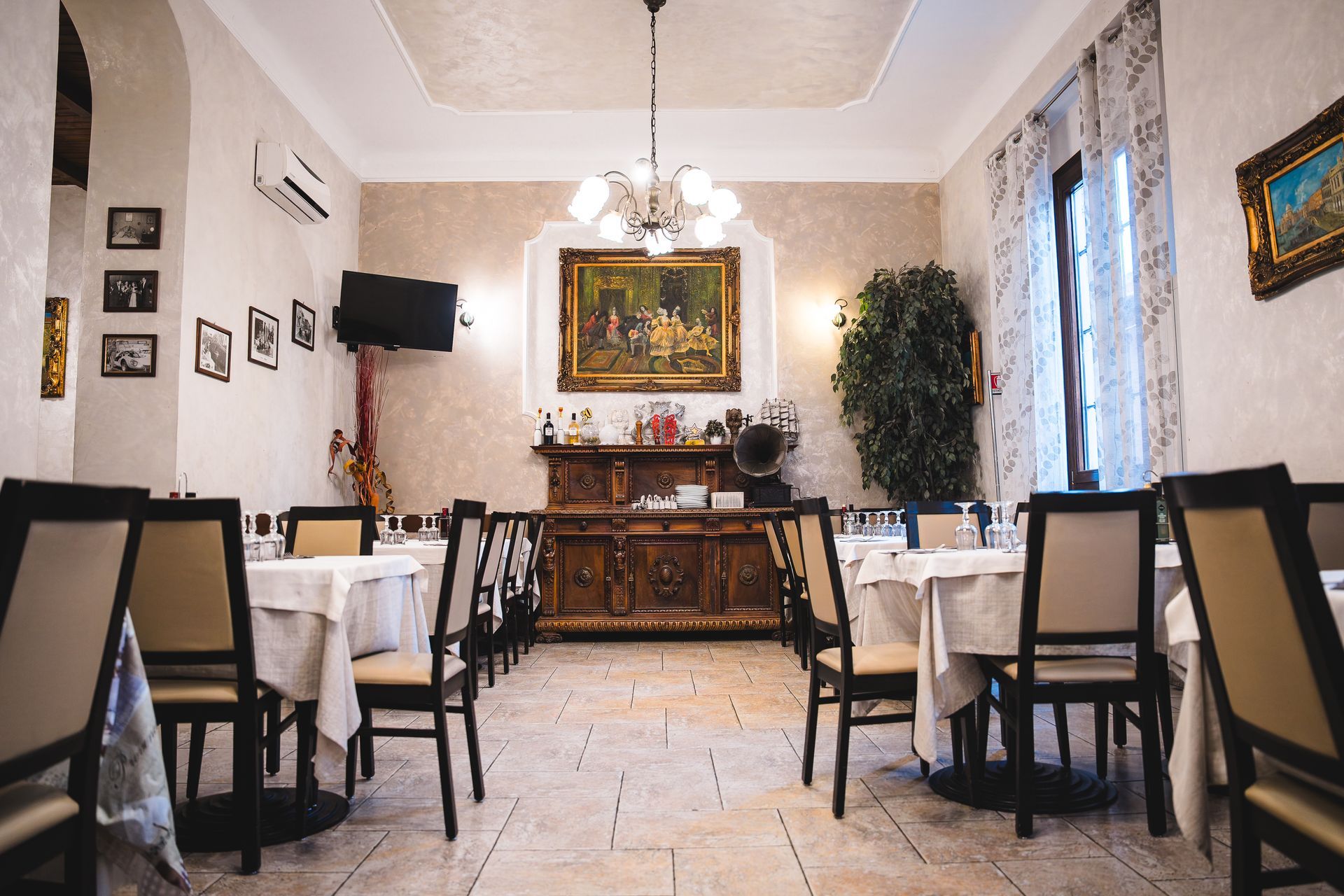 Sala da pranzo del ristorante con tavoli apparecchiati per gli ospiti, lampadario, buffet e quadri incorniciati.