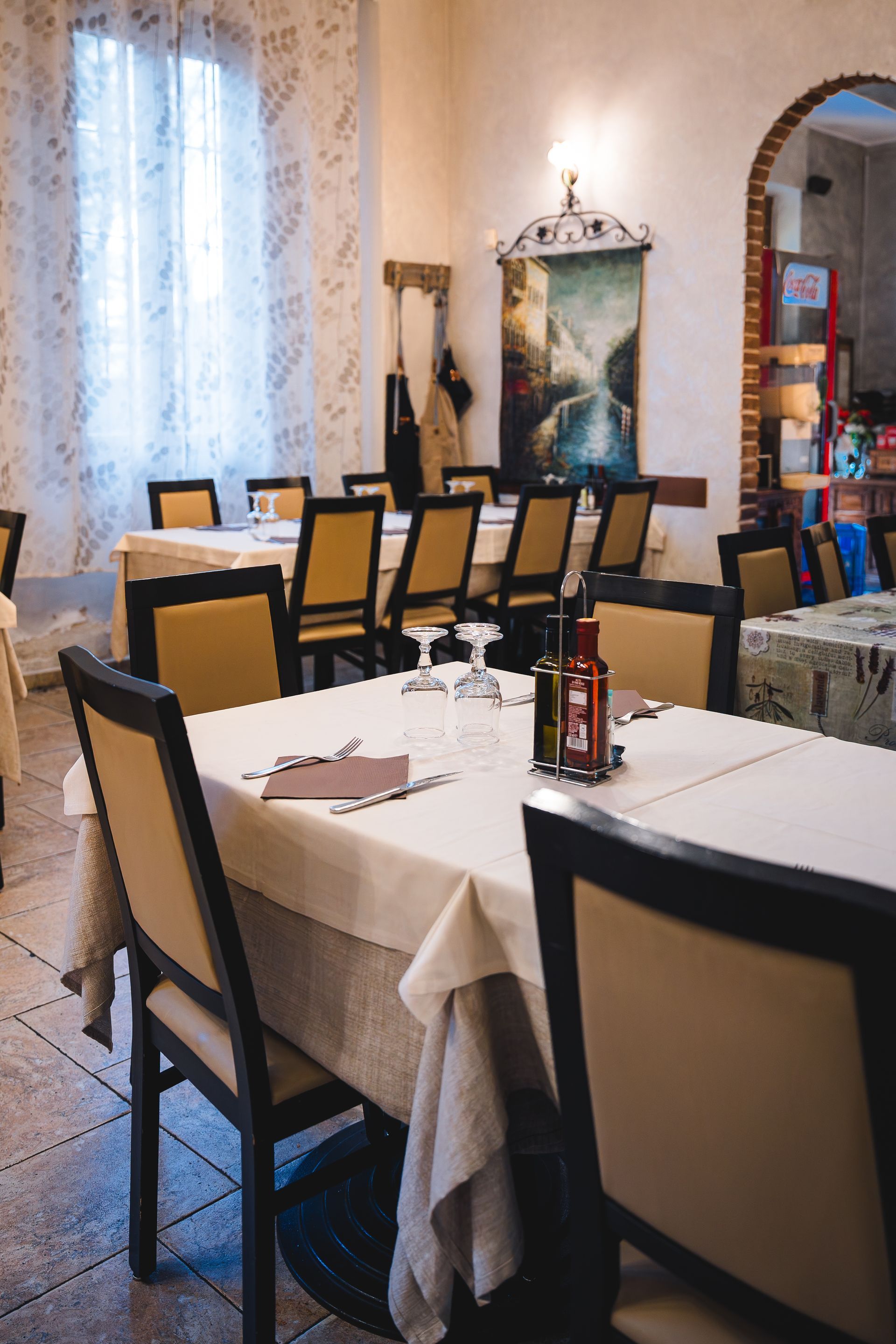 Sala da pranzo del ristorante con tavoli apparecchiati per il servizio, tovaglie, sedie e decorazioni beige.