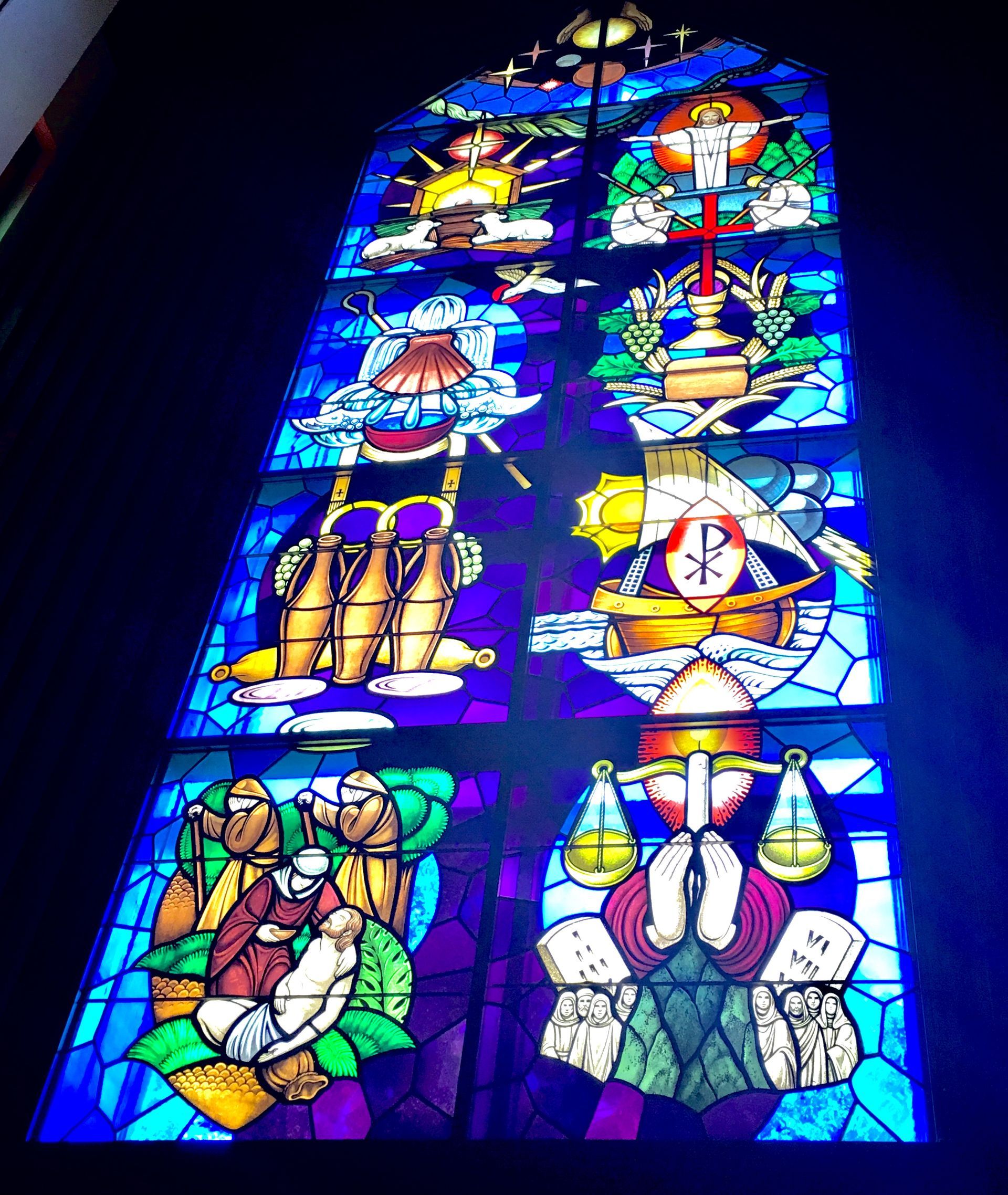 Colorful stained-glass panel with religious symbols and figures in blue, green, yellow, and red.