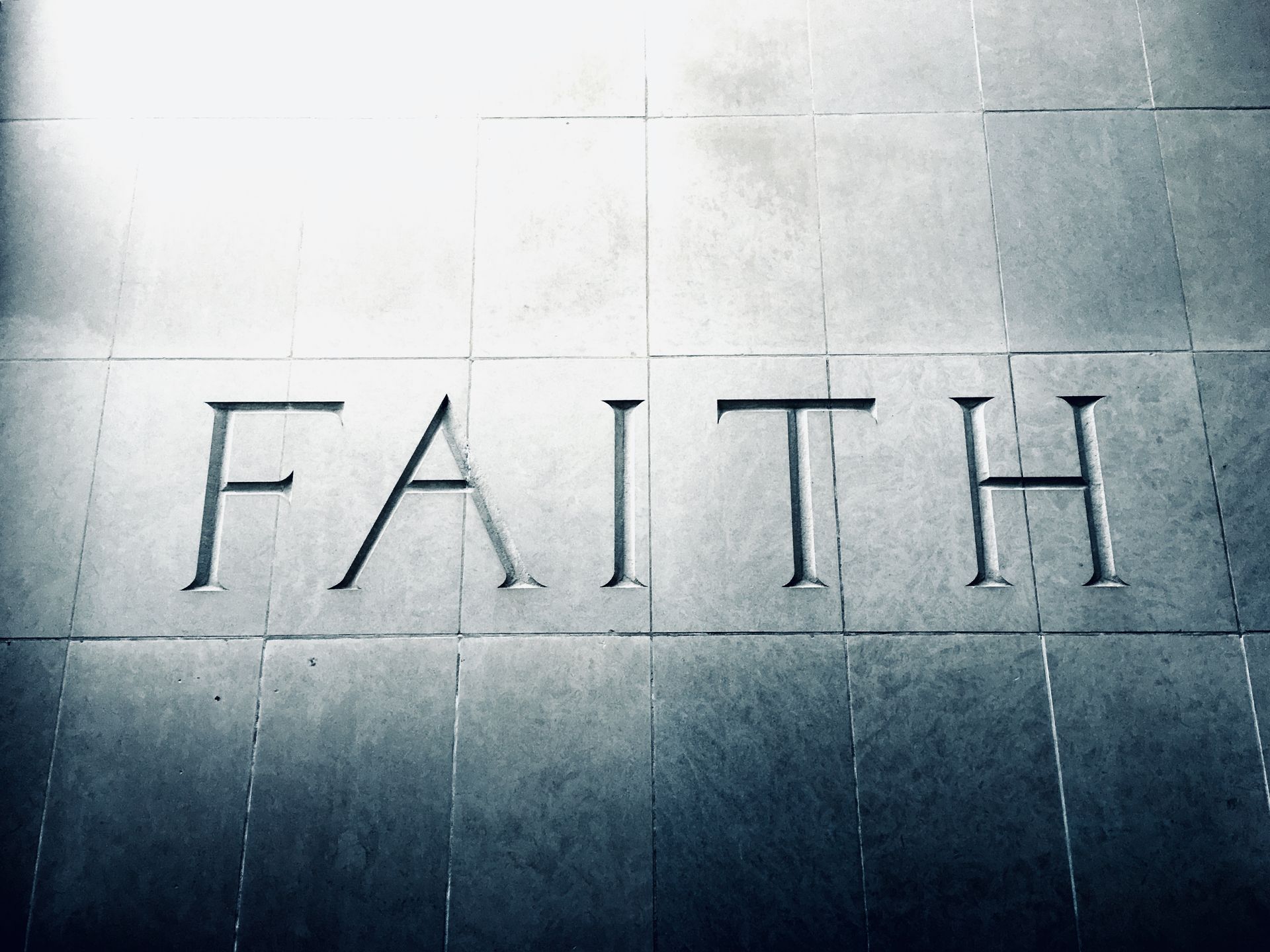 The word “FAITH” carved into a gray stone surface.