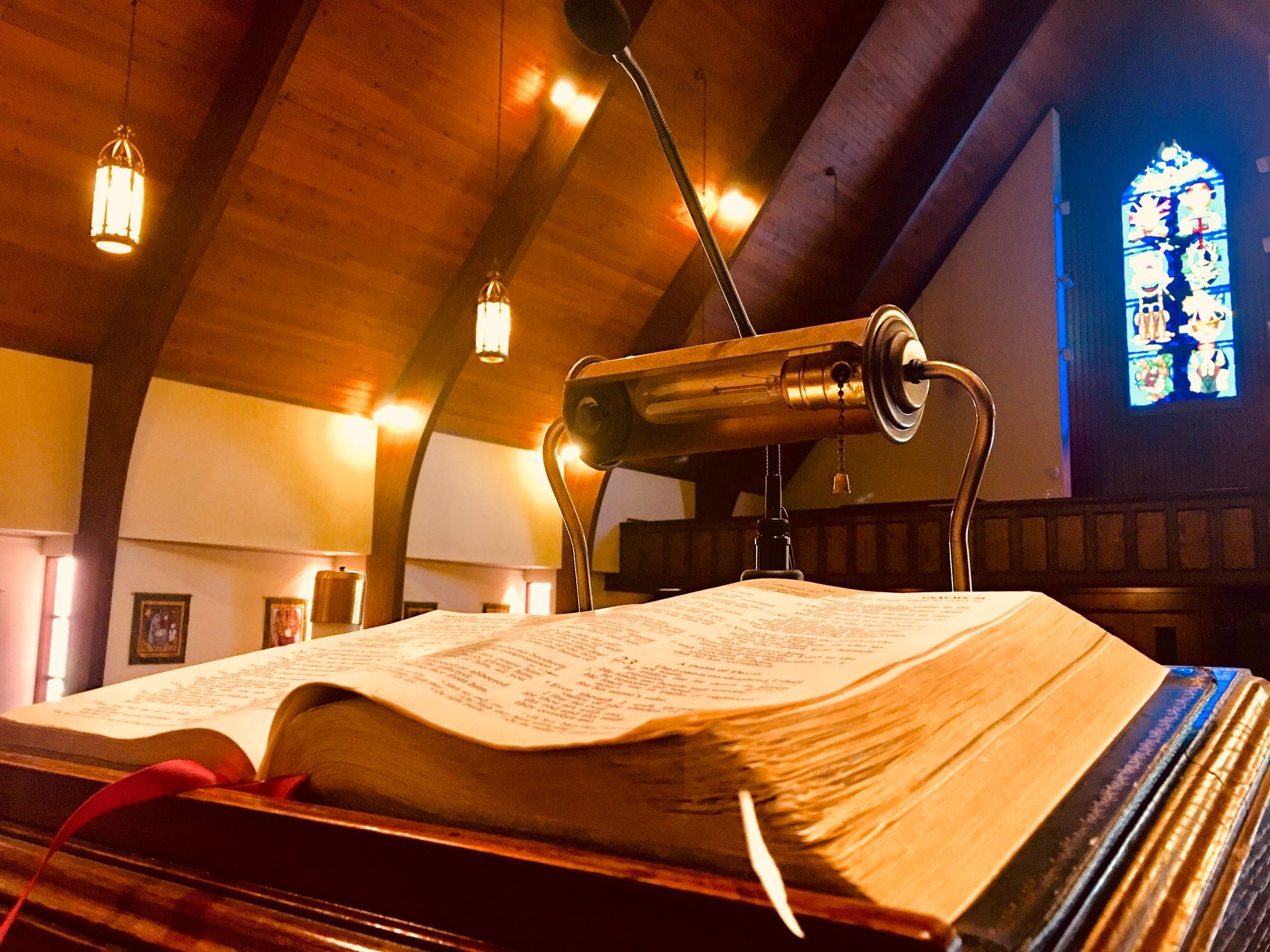 Open Bible on a church lectern beneath warm lights and stained glass.