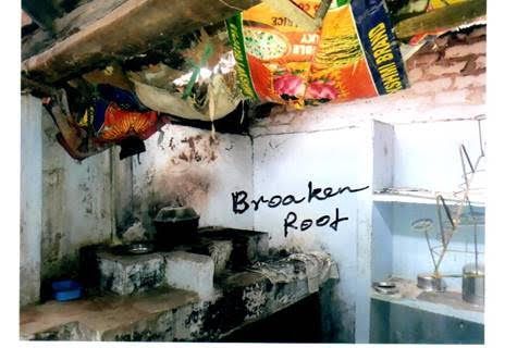 Broken-roof room with peeling walls, exposed beams, hanging fabric, and a sink on the right.