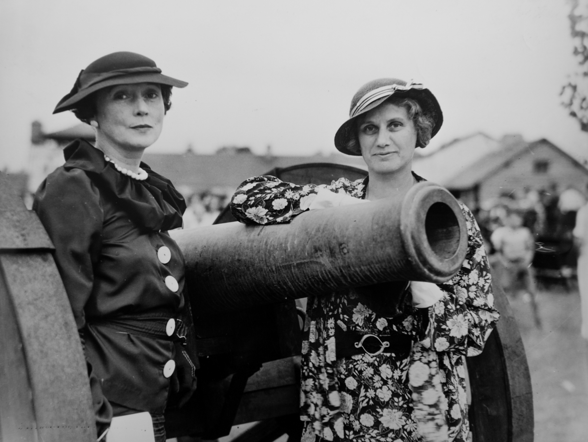 Two women standing next to a cannon in a black and white photo