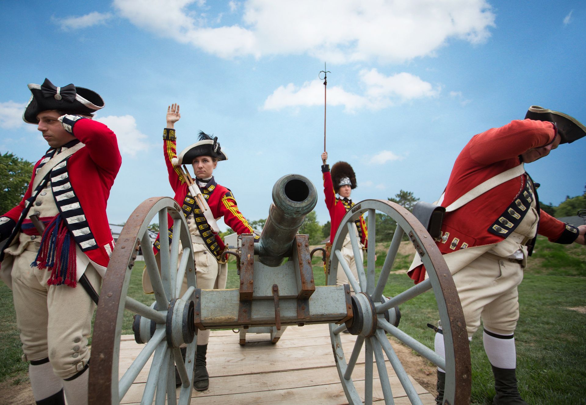 A group of men in military uniforms are standing around a cannon.