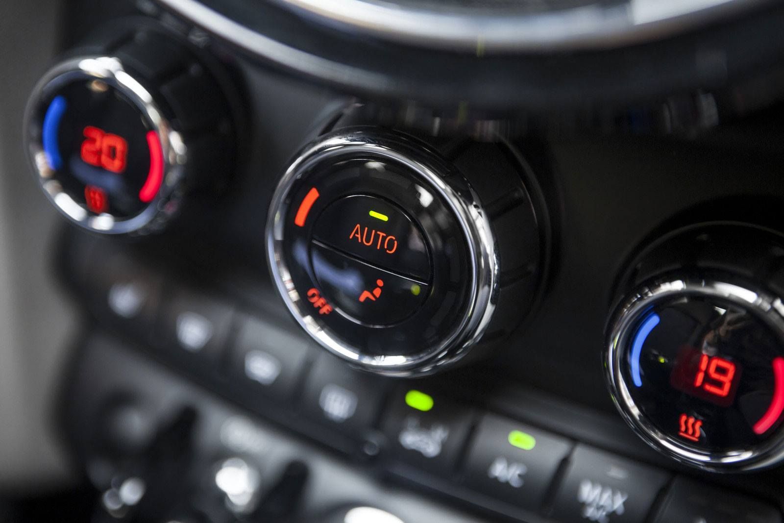 Car's climate control panel with three round dials. The center dial says 