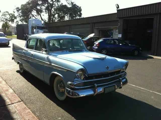 Light blue vintage car with chrome accents parked on asphalt. White-walled tires.