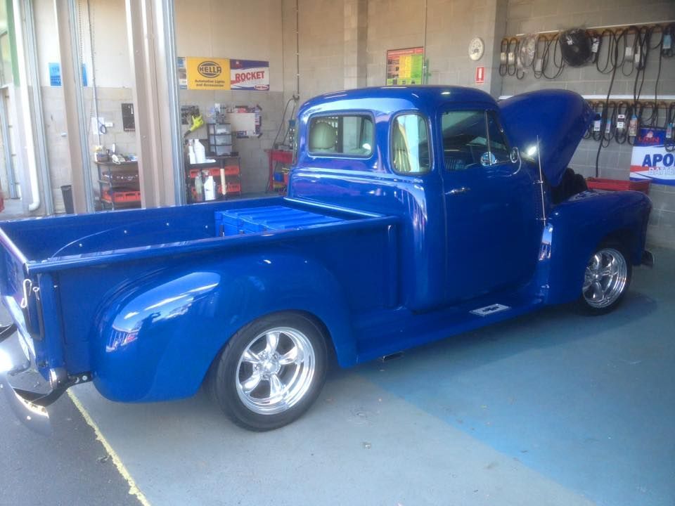 Blue classic pickup truck with hood up in a garage.