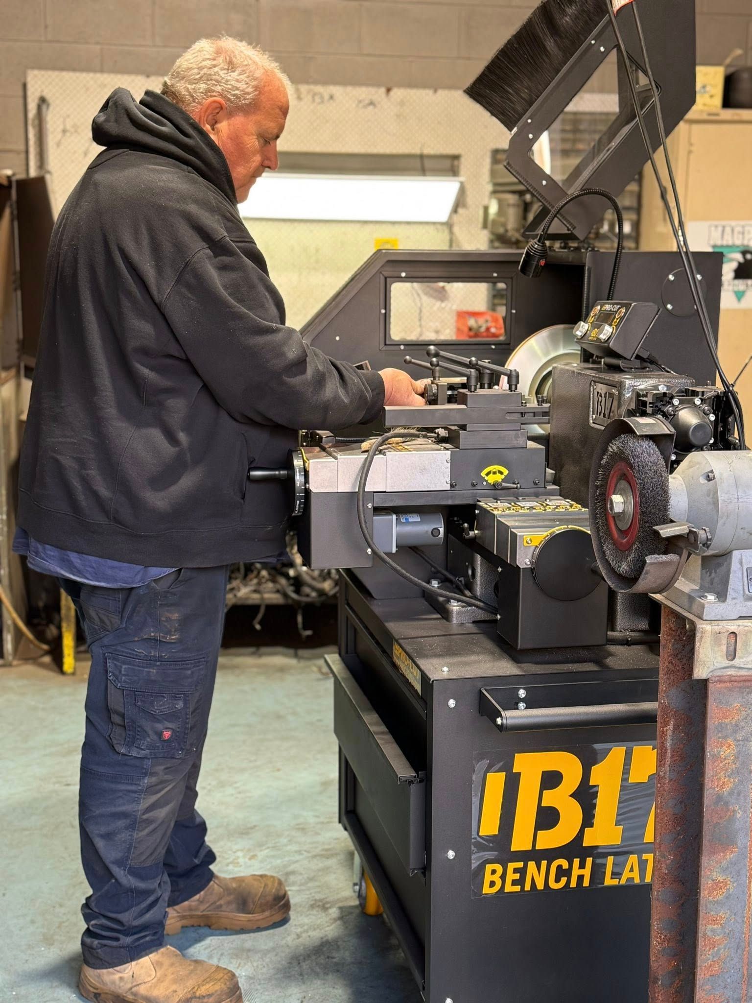 Man using a bench lathe, wearing work clothes, in a workshop.