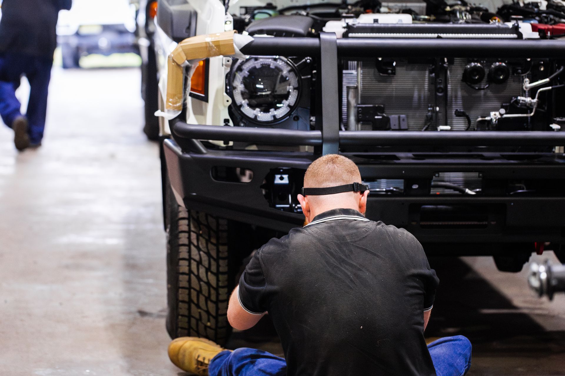 A mechanic is performing a 4WD accessory fitting, installing a bull bar onto a vehicle.