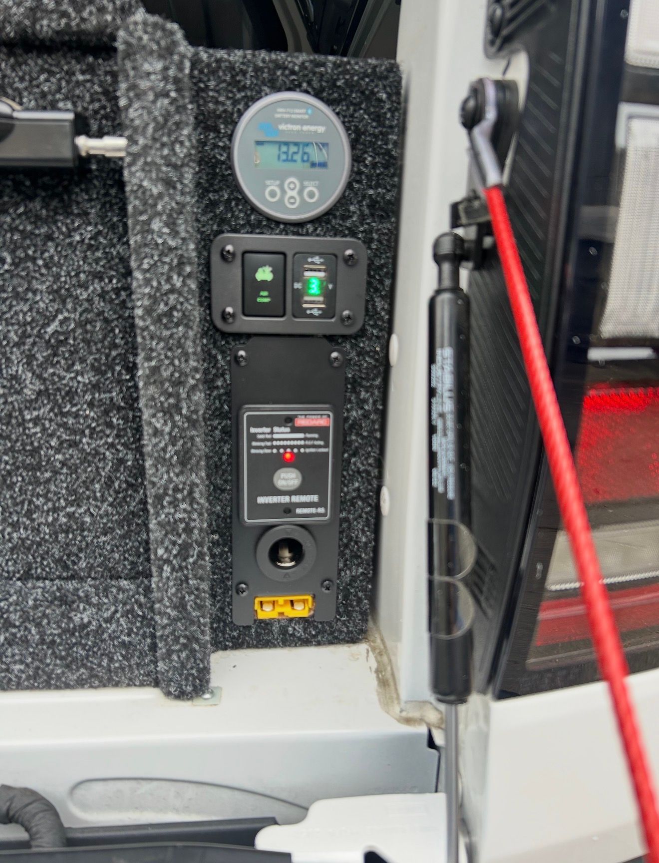 A vehicle's interior showing a power control panel with a digital display, switches, and a 12V outlet.