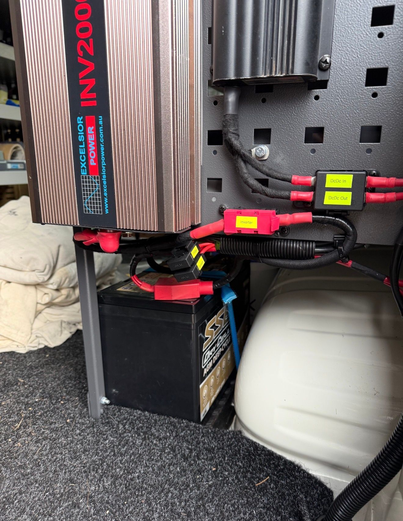 Battery connected to an inverter, mounted in a vehicle. Red and black cables, with fuses.