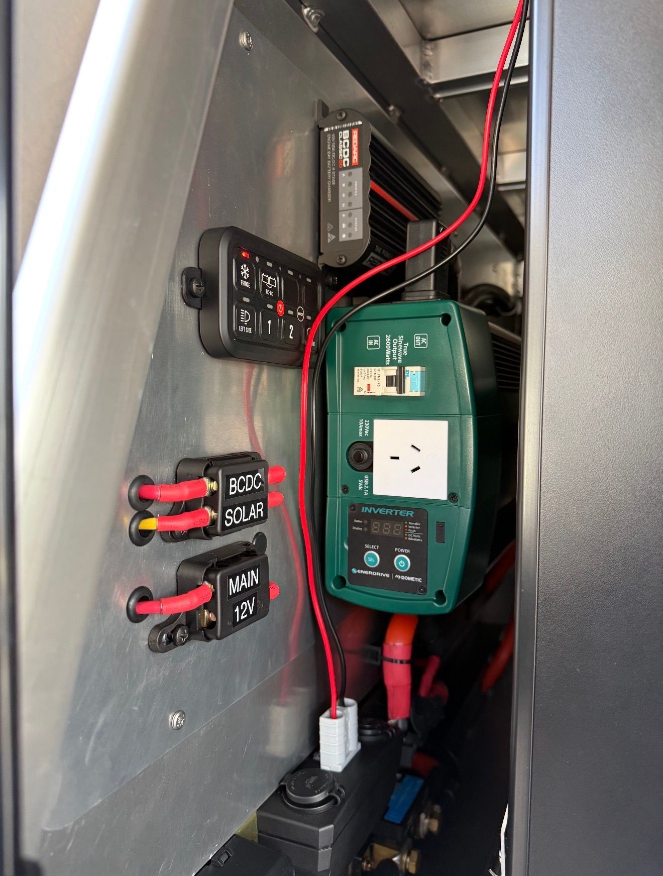 Electrical components mounted in a vehicle: switch panel, power inverter, and wiring on a metal panel.