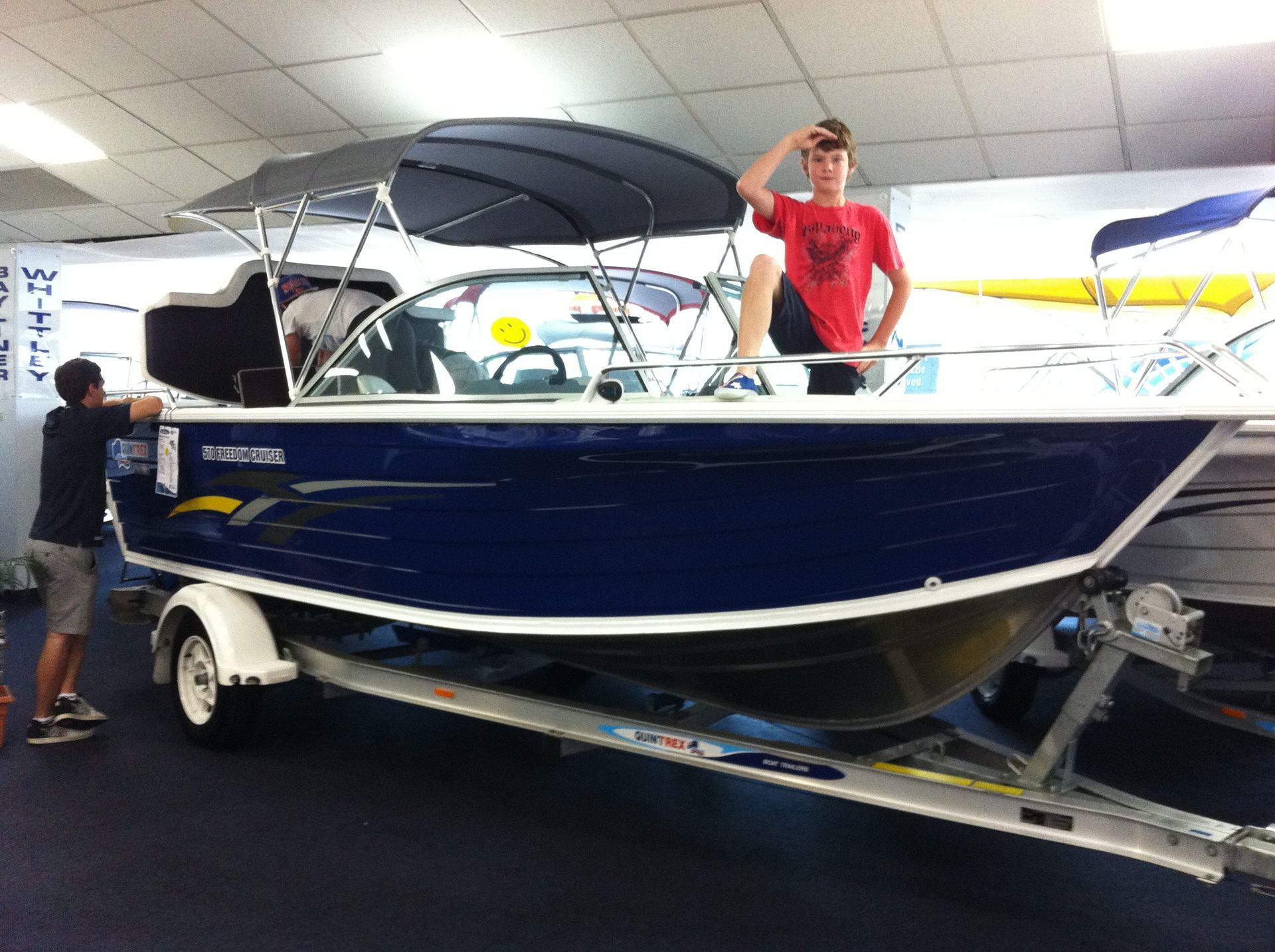 Woman seated at an office desk, smiling, holding a card. She's wearing a black top and jeans.