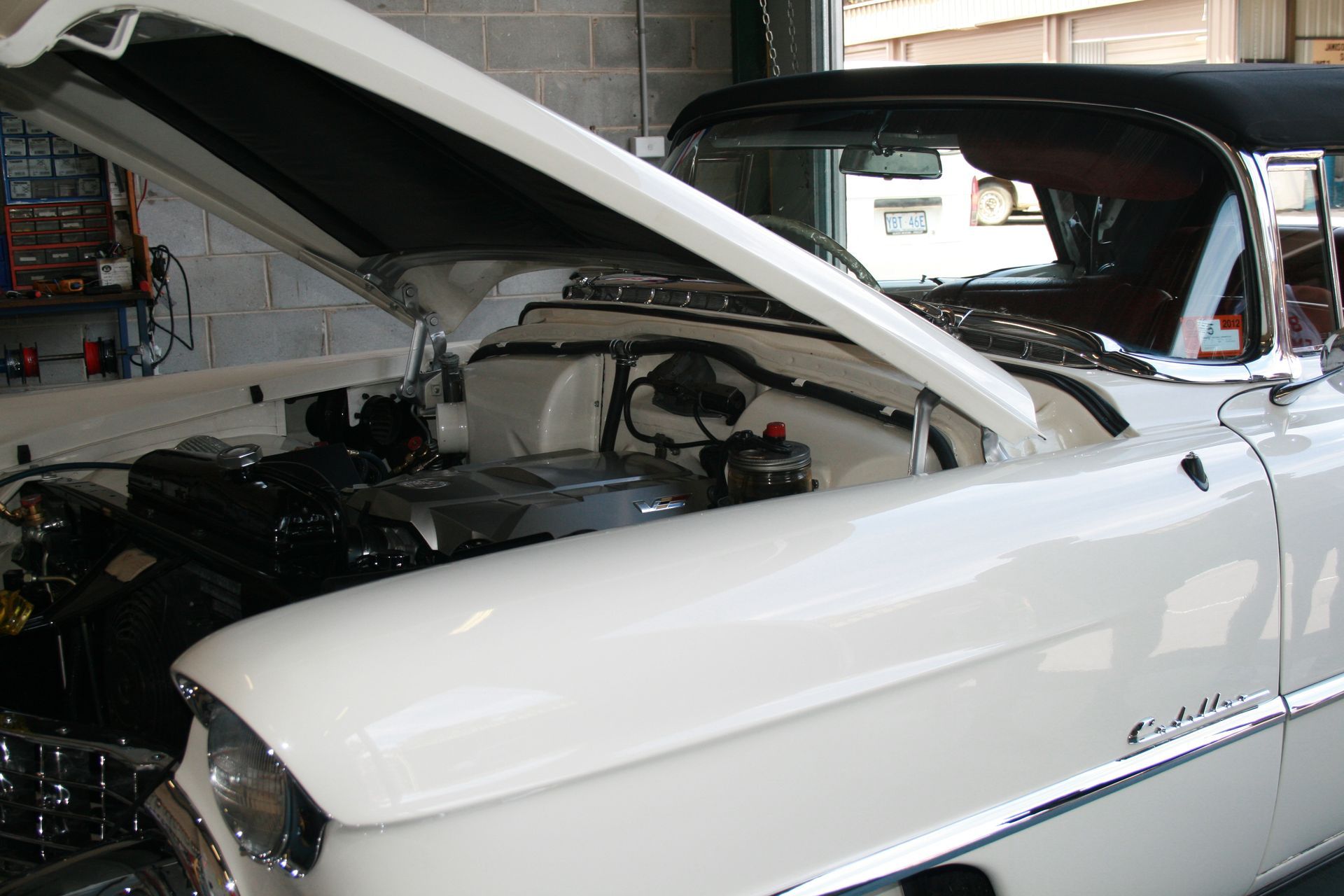 White classic Cadillac with hood open, showing engine. Interior of garage visible.