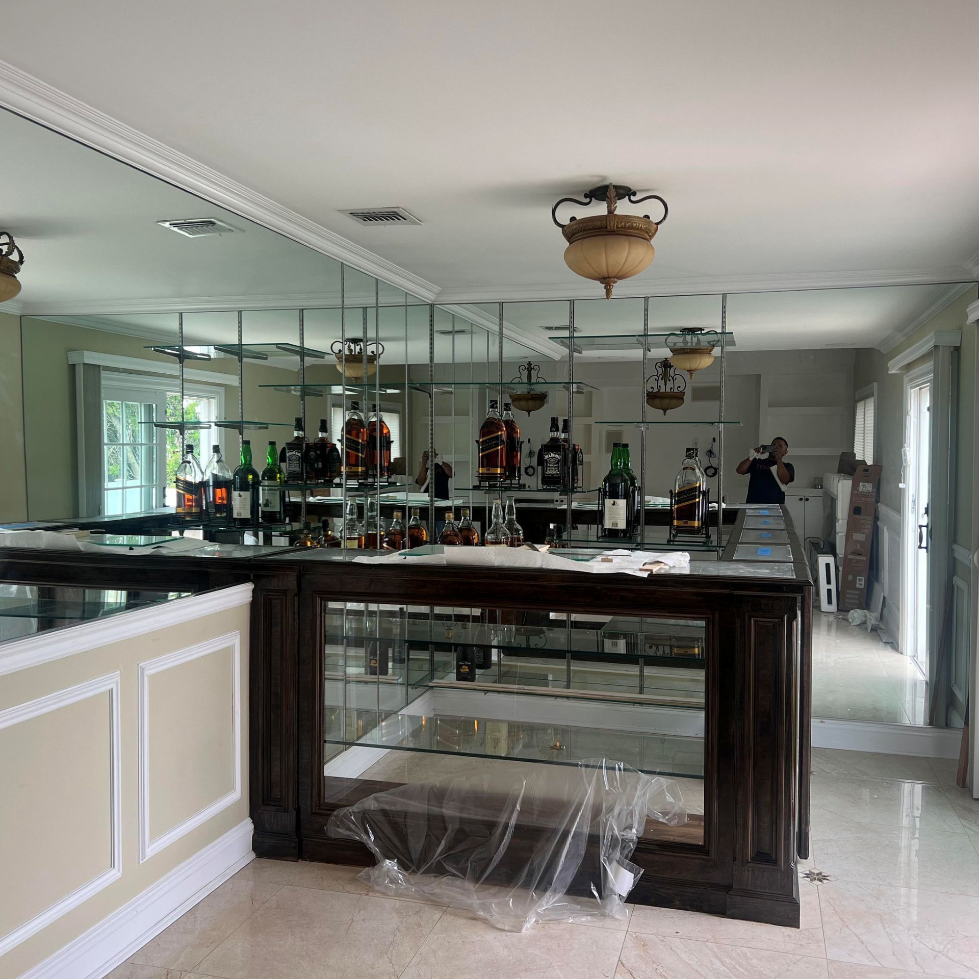 A home wet bar with a wooden counter, glass shelves, and a large mirrored wall reflecting the room.
