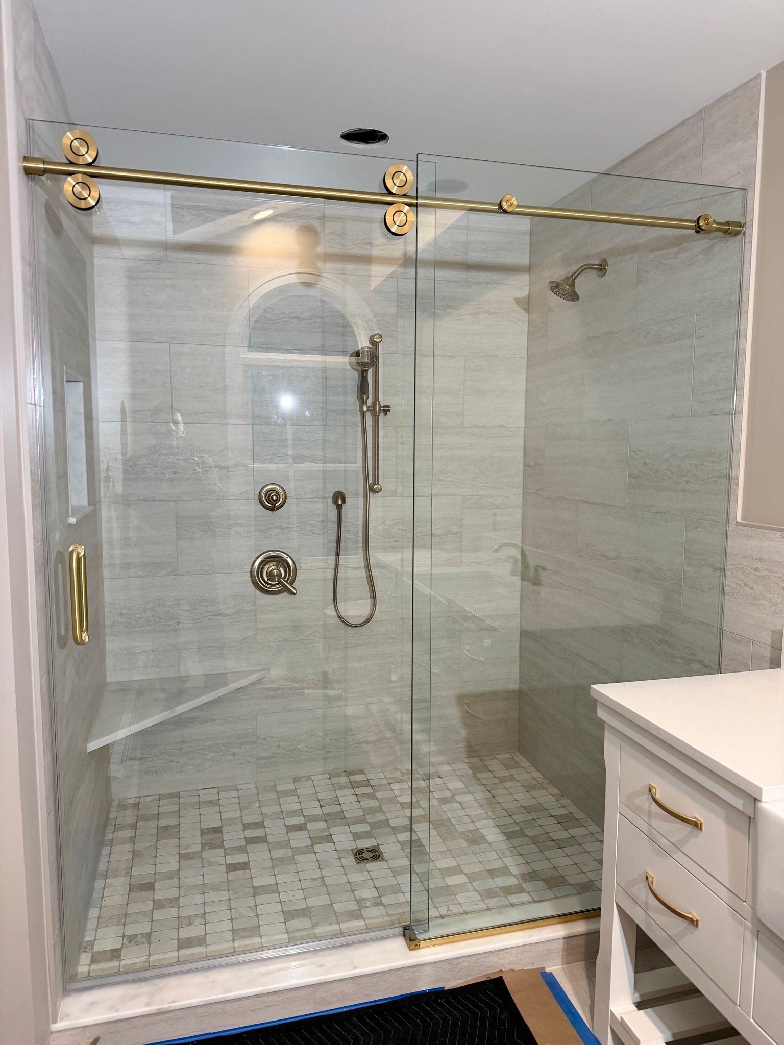 A modern walk-in shower with gold hardware, a glass sliding door, marble-tiled walls, and a built-in corner bench.