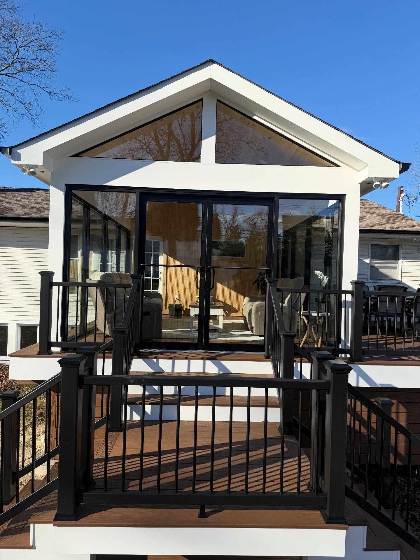 Sunroom addition with black-framed glass doors and windows, featuring a front deck with black railings and stairs.
